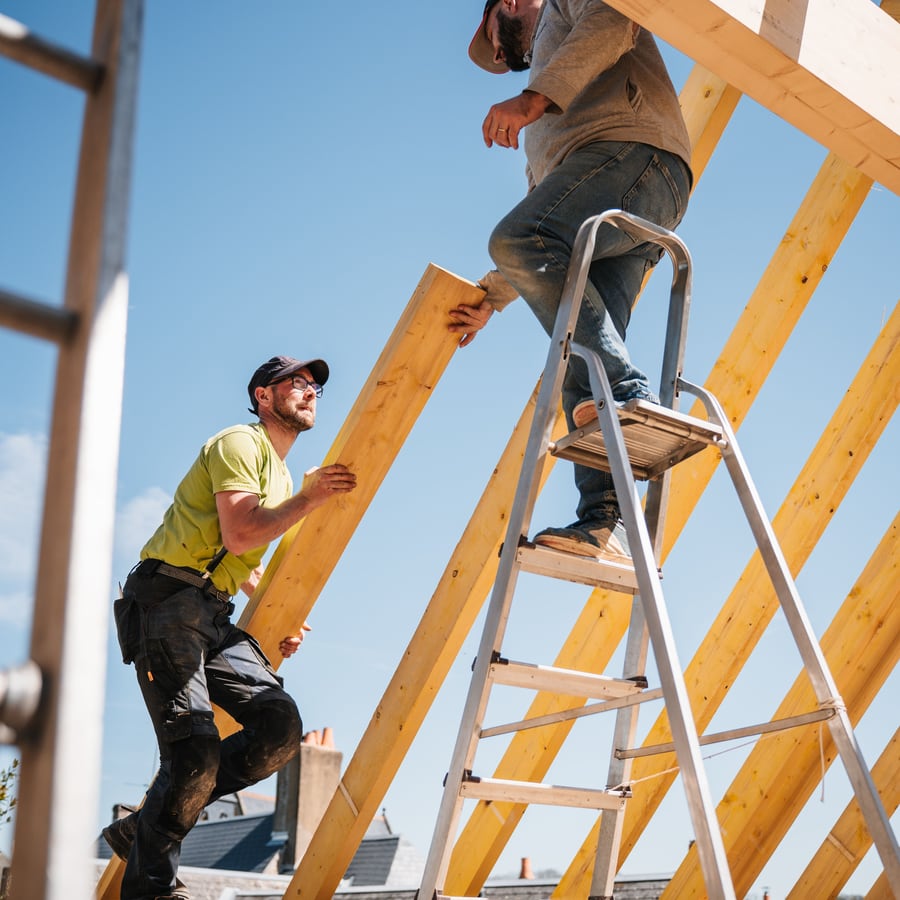 Zwei Dachdecker heben eine Holzbohle auf den Dachstuhl