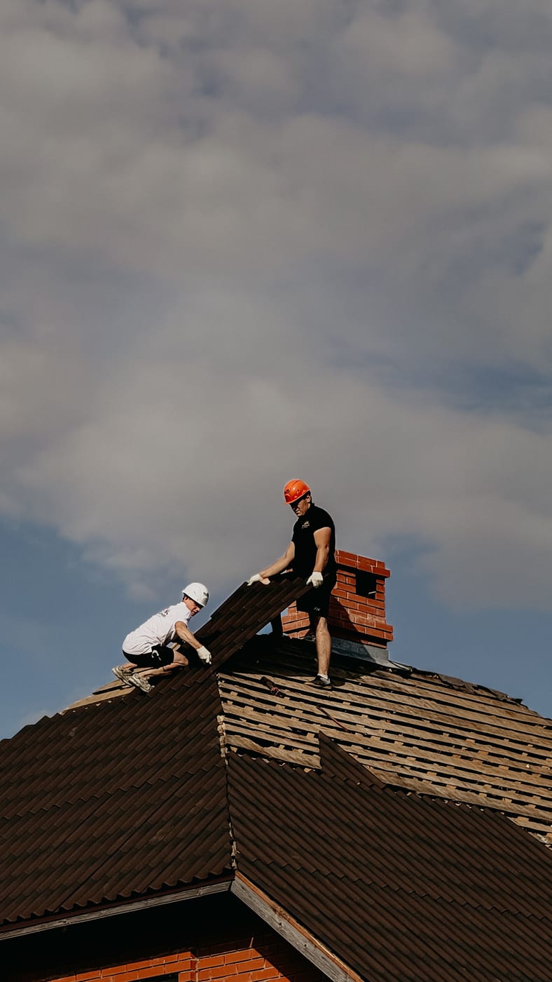 Zwei Dachdecker setzen Firstziegel auf einem frisch eingedeckten Steildach